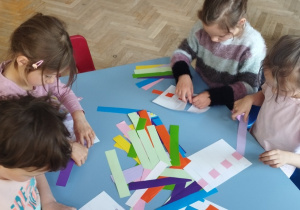 Grupa dzieci przeplata kolorowe paski.