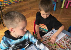 Chłopcy szukają danych produktów w gazetach.