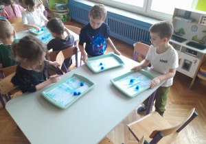 Dzieci malują kartkę kostkami lodu