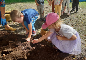 Dzieci sadzą cebulki kwiatowe na rabatce