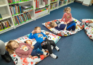 Dzieci siedzą i leżą na pufach i słuchają czytanej książki