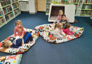 Dzieci siedzą i leżą na pufach i słuchają czytanej książki