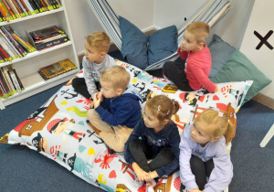 Dzieci siedzą na pufach i słuchają czytanej książki