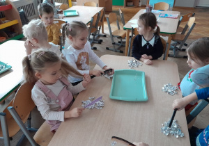 Dzieci eksperymentują z naelektryzowanym grzebieniem i kawałkami folii aluminiowej