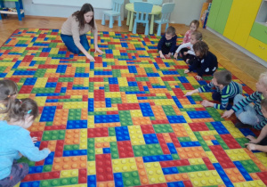 Dzieci kreślą na dywanie literę "d"