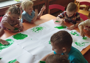 Dzieci malują palcami zieloną farbą.