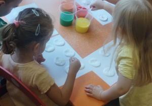 Dzieci pipetą nakładają farbę na płatki kosmetyczne.