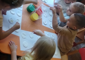 Dzieci pipetą nakładają farbę na płatki kosmetyczne.