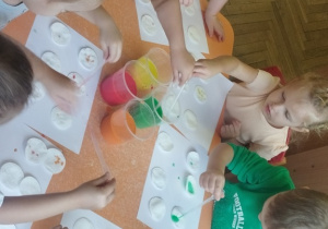 Dzieci pipetą nakładają farbę na płatki kosmetyczne.