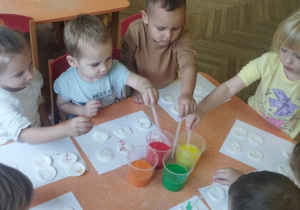 Dzieci pipetą nakładają farbę na płatki kosmetyczne.