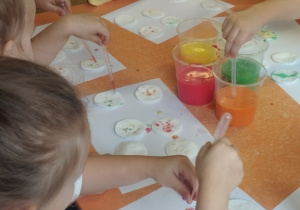 Dzieci pipetą nakładają farbę na płatki kosmetyczne.
