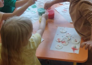 Dzieci pipetą nakładają farbę na płatki kosmetyczne.
