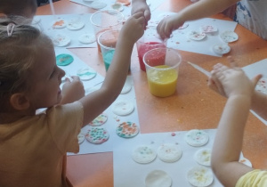 Dzieci pipetą nakładają farbę na płatki kosmetyczne.