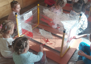 Grupa dzieci maluje na folii farbą flagę Polski.