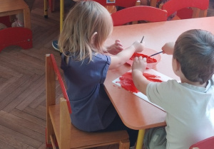 Dzieci malują kartki papieru czerwoną farbą.