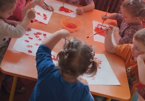 Grupa dzieci maluje czerwoną kartką kartki papieru.