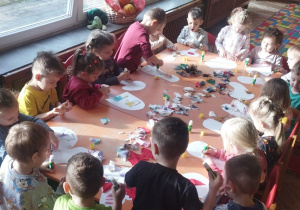 Grupa dzieci wykleja prace materiałami.