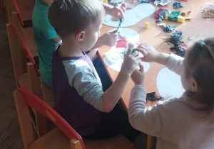 Grupa dzieci wykleja prace materiałami.