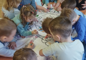 Grupa dzieci koloruje kolorowankę prawa dziecka.