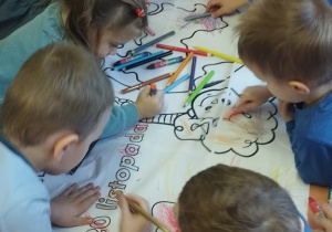 Grupa dzieci koloruje kolorowankę prawa dziecka.