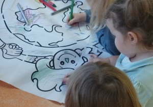 Grupa dzieci koloruje kolorowankę prawa dziecka.