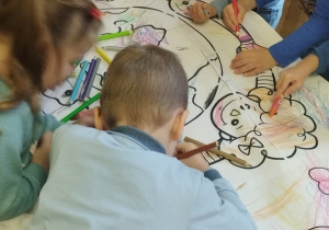 Grupa dzieci koloruje kolorowankę prawa dziecka.